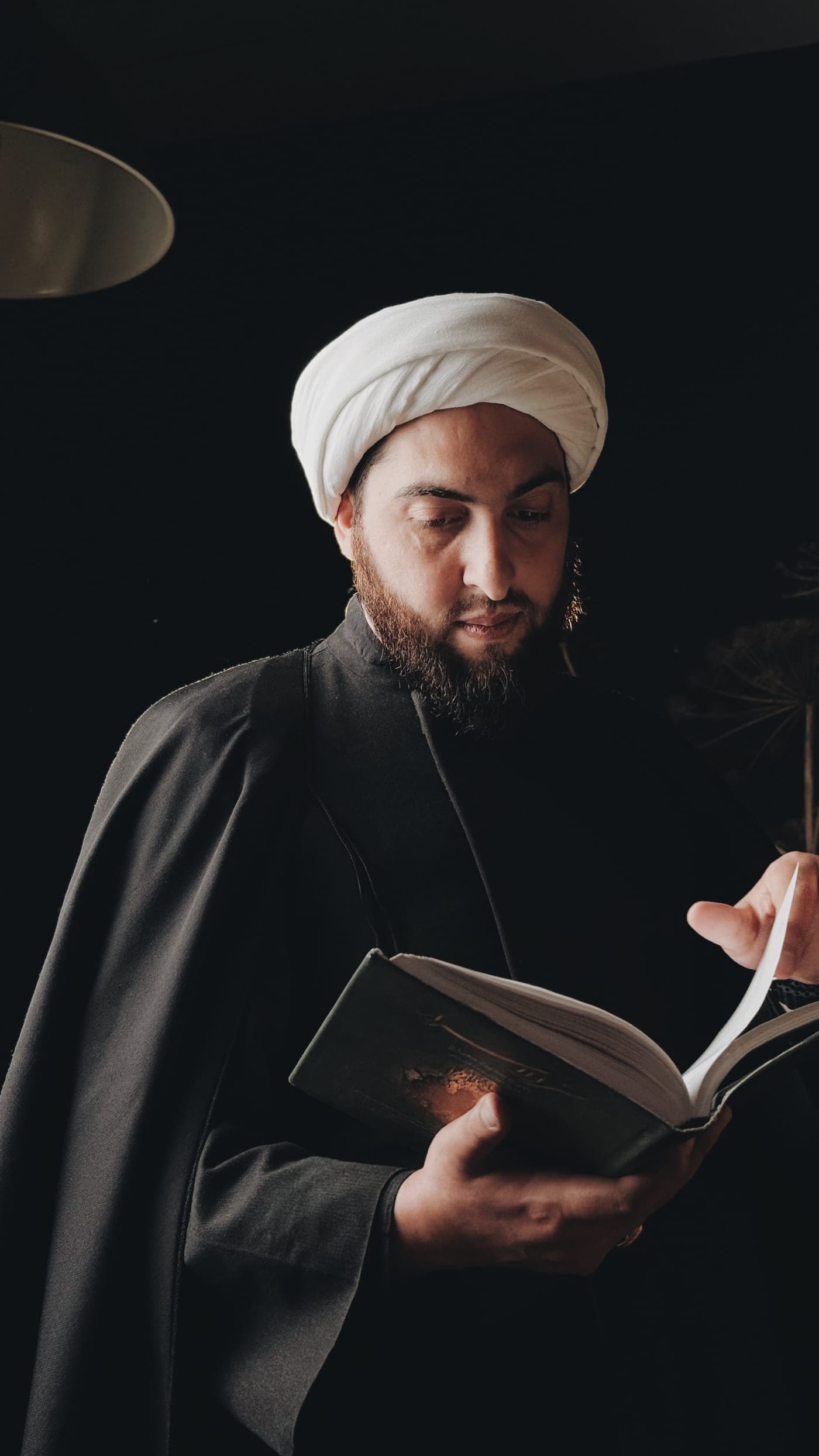Учитель Хусейн читает раскрытую книгу у лампы